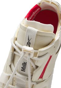 Baskets en cuir blanc avec des accents rouges, lacets élastiques et une languette rembourrée. Comprend une semelle intérieure rembourrée et une surface texturée.