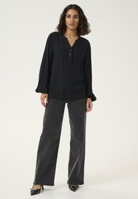 Haut noir à manches longues avec un col henley boutonné, associé à un jeans large noir foncé taille haute et des chaussures à talons noires.
