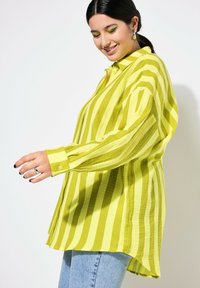 Camicia a maniche lunghe, con bottoni, di un brillante colore giallo con righe verticali. Tessuto testurizzato con una vestibilità rilassata, orlo arrotondato e polsini abbottonati.