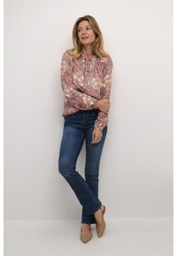 Blouse à motifs avec des nuances de rose, d'orange et de blanc, assortie à un jean en denim bleu et des escarpins beiges à bout pointu.