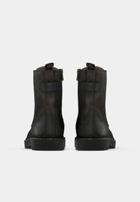 Botines de cuero negro con acabado texturizado, con cremalleras laterales y una suela negra resistente. Diseño simple sin patrones visibles.