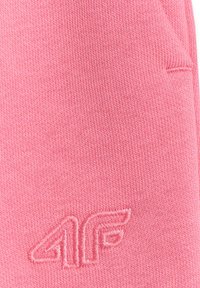 Gros plan sur un tissu tricoté rose avec un logo brodé en relief "4F" dans une couleur de fil assortie en bas à droite.