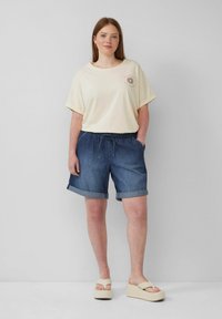 T-shirt ample jaune clair avec un graphique de soleil sur la poitrine, associé à un short en denim retroussé et des sandales à plateformes beiges.