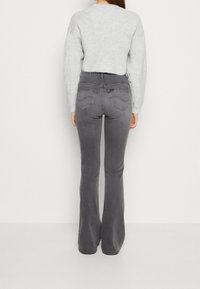 Jeans acampanados grises de denim, con un diseño de cintura alta, bolsillos traseros con detalles de costura y una textura suave.
