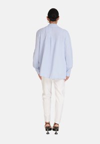Camicia in misto cotone blu chiaro con una vestibilità comoda, maniche lunghe e schiena plissettata, abbinata a pantaloni bianchi e scarpe nere con tacco.