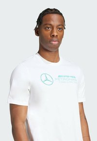 Camiseta de algodón blanca con un logo turquesa del equipo AMG Petronas de Fórmula Uno y un emblema de estrella de Mercedes-Benz en la parte frontal.