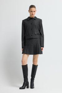Grijze jas met een zwarte kraag en knopen, gecombineerd met een geplooide minirok. Zwarte leren kniehoge laarzen met een vierkante hak.