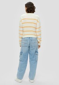 Gestreifter Strickpullover in Creme und Orange, kombiniert mit lichtblauen Cargo-Hosen mit Taschen. Der Pullover hat einen gerippten Halsausschnitt und einen gerippten Saum.
