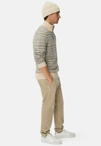 Beige gebreide trui met een hoge kraag en ritsdetail, uitgerust met geometrische patronen. Gecombineerd met beige corduroy broek en witte sneakers.