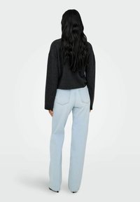 Maglione oversize nero abbinato a jeans a vita alta blu chiaro a gamba dritta. Capelli lunghi e ondulati visibili mentre il soggetto è girato di spalle.