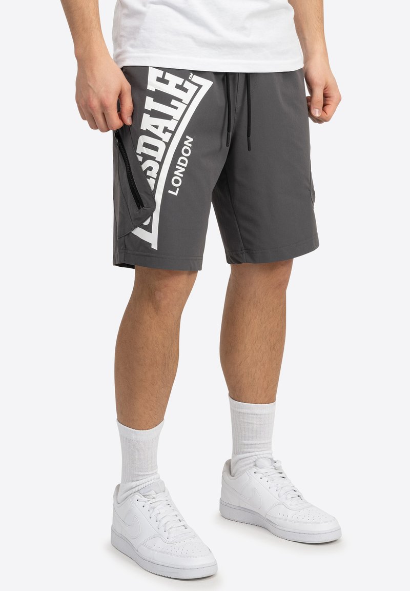 Pantaloni corti grigi con una grafica bianca che presenta "Lonsdale" e "London". Include una tasca laterale con zip, coulisse nera e tessuto liscio.