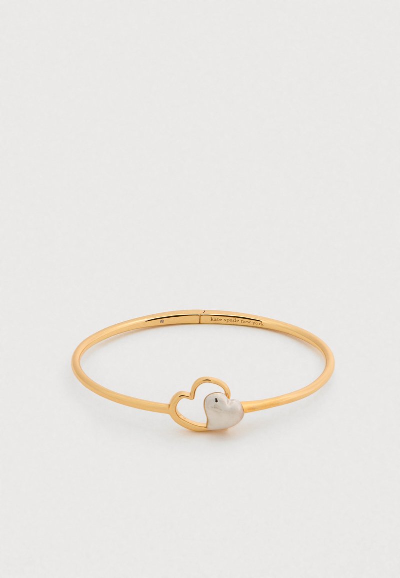 Βραχιόλι βέργα από μεταλλικό υλικό σε χρυσό χρώμα με σχέδιο διπλής καρδιάς και λευκή καρδιά ως διακριτικό. Λεπτή υφή, ανοιχτού τύπου σχεδιασμός.