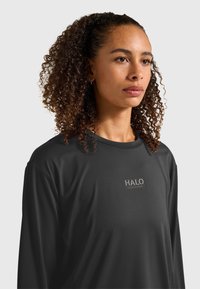 Czarna koszula z długim rękawem wykonana z gładkiej tkaniny, z szarym logo. Koszula ma luźny krój i okrągły dekolt.