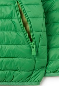 Grüne, puffige Jacke mit glatter Oberfläche und einem großen seitlichen Reißverschluss. Das Innere hat einen helleren Grünton und ist mit einem gesteppten Muster versehen.