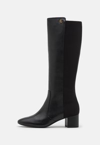 Bottes noires hautes jusqu'au genou avec un bout pointu, présentant un design en cuir et en élastique, un talon carré et un petit logo doré.