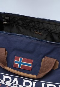 Laivaston värinen kangaskassi ruskeilla kahvoilla, jossa on vetoketjusulku, musta sisus ja brodeerattu Islannin lipun merkki edessä.