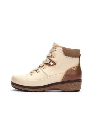Botas de tobillo beige y marrón con un upper de cuero texturizado, herrajes dorados y una suela rugosa. Presentan materiales en contraste y un ligero tacón.