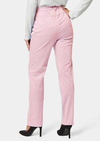 Roze, rekbare broek met een relaxte fit en elastische tailleband, gedragen met zwarte hoge hakken, die een gladde textuur en op maat gemaakt ontwerp laten zien.