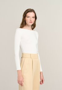 Long-sleeved white top with a boat neckline, paired with high-waisted beige trousers featuring front pleats and a tailored design.