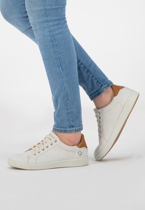 Weiße Wildledersneaker mit einem akzentuierten Absatz aus braunem Leder, Schnürdesign und strukturiertem Gummisohle, kombiniert mit blauen Slim-Fit-Jeans.