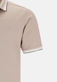 Polo beige con maniche corte, tessuto texturizzato e colletto a tre bottoni. Presenta dettagli a strisce bianche e nere sul colletto.