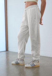 Ljusgråa mjukisbyxor med elastiska muddar, dragsko i midjan och sidofickor. Kombinerade med grå och cremefärgade sportskor med blå detaljer.