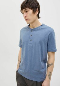 Tarkék, rövid ujjú henley póló, puha anyagból, kerek nyakkivágással, három sötét gombbal és laza szabással.