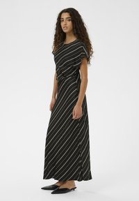 Must mustriga kleit valgete diagonaaljoontega, lühikesed varrukad ja nööri vöödetail. Mudel kannab musti terava ninaga kortereid. Sujuv kangas.