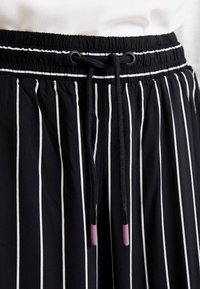 Svartvita randiga byxor med elastisk midja. Har en dragsko med lila detaljer och en mjuk, lätt tygkvalitet.