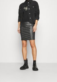 Black denim jacket, black sweatshirt with logo, shiny black pencil skirt, and black ankle boots. Focus on texture and metallic sheen of the skirt.