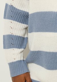 Niebiesko-biały sweter w paski z teksturowanym wzorem dzianiny, z długimi rękawami i otwartymi detalami wzdłuż szwu.