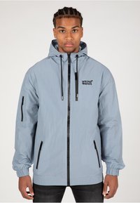 Hellblaues Jackett mit Kapuze, elastischen Bündchen und Reißverschlusstaschen. Mit schwarzem Logodetail und Frontreißverschluss. Glatte Textur.