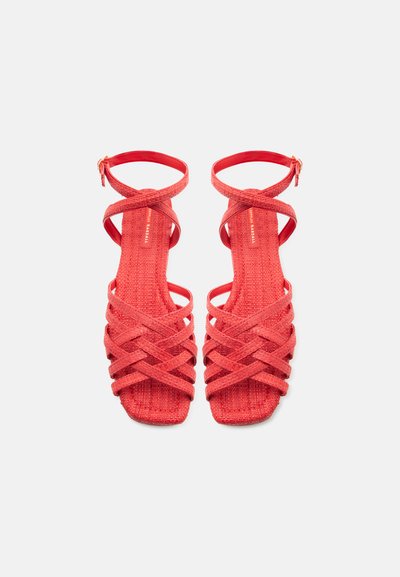 Κόκκινα υφαντά σανδάλια με λουράκια και αγκράφες στον αστράγαλο, σχέδιο με τετράγωνη μύτη και σταυρωτό μοτίβο πάνω στην πατούσα, φαίνονται από πάνω σε λευκό φόντο.