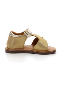 Sandalia dorada con un acabado brillante, diseño de punta abierta, correa ajustable con hebilla y suela plana marrón. Textura suave y estilo minimalista.
