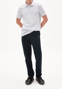 Ljusgrå pikétröja med korta ärmar och klassisk krage, kombinerad med mörkblå chinos och svarta skor. Enkel design med minimala detaljer.