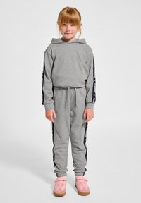 Grå hoodie och joggingset med svarta sidopaneler som har vit text. Bärs med rosa sneakers och dragsko i midjan. Slät textur.