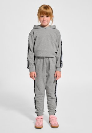 Grauer Hoodie und Jogginganzug mit schwarzen Seitestreifen und weißem Text. Getragen mit rosa Sneakers und elastischem Bund mit Kordelzug. Glatte Textur.