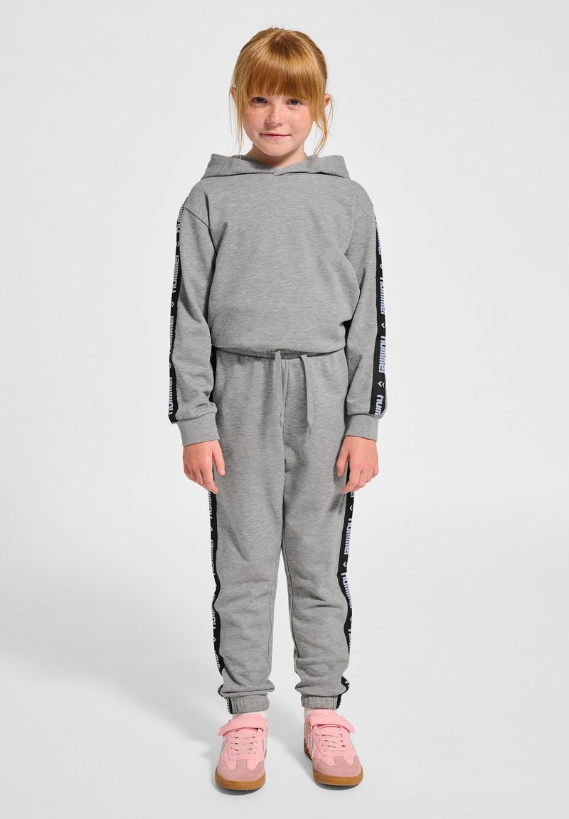 Grå hoodie och joggingset med svarta sidopaneler som har vit text. Bärs med rosa sneakers och dragsko i midjan. Slät textur.