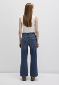 Wide-leg blue denim jeans with a high waist, featuring standard back pockets and a clean finish at the hem, paired with a fitted white top.