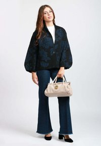 Cardigan oversize nero con motivo floreale e chiusura con bottoni, abbinato a jeans svasati blu e una borsa beige chiaro. Scarpe nere completano l'outfit.