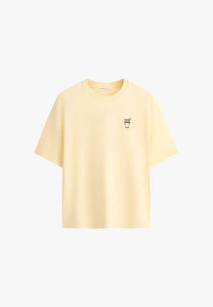 Hellgelbes kurzärmeliges T-Shirt mit Rundhalsausschnitt und kleinem schwarzem Umriss eines Getränks mit Strohhalm und Garnitur auf der linken Brust.