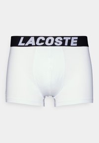Boxeri albi din bumbac cu un elastic negru la talie, pe care este imprimat "LACOSTE" în alb. Material neted, design ajustat, lungime medie până la coapsă.