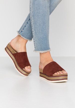 Brown suede platform sandals with an open toe, featuring a textured cork midsole and colorful woven accents at the base.