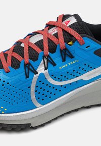 Scarpa da trail running Nike blu con tomaia in mesh traspirante, lacci rossi, dettagli argentati e suola testurizzata per una migliore aderenza.