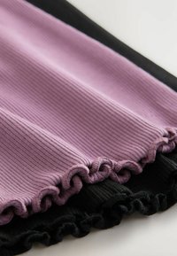 Ribbade tyger i lavendel och svart, med volangkanter. Den strukturerade ytan tillför djup åt färgerna och betonar de kontrasterande nyanserna.