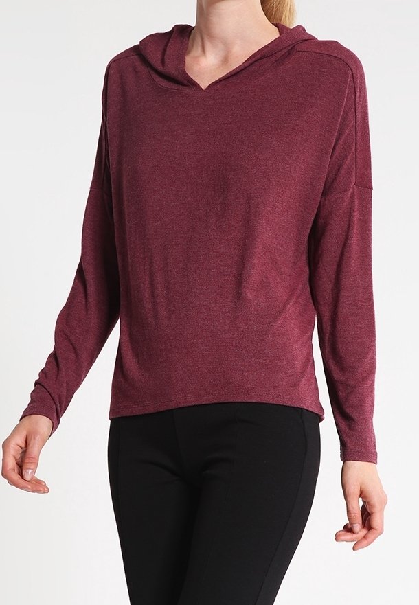 Burgundy long-sleeve hoodie with a v-neck and relaxed fit. Soft fabric with dropped shoulders. Paired with black pants.
