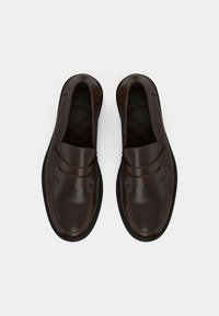 Mocassins en cuir marron avec une finition brillante, présentant un accent cousu sur la tige et une semelle en caoutchouc. Sans lacets.