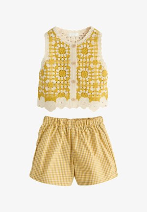 Hæklet ærmeløs vest med gult og cremefarvet blomsterprint og træknapper, kombineret med gule gingham-shorts med elastik i taljen.