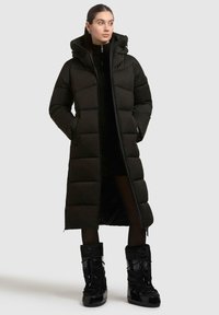 Sort puffet frakke med lang design, quiltet tekstur, høj krave og lynlåslommer. Krydret med skinnende sorte vinterstøvler.