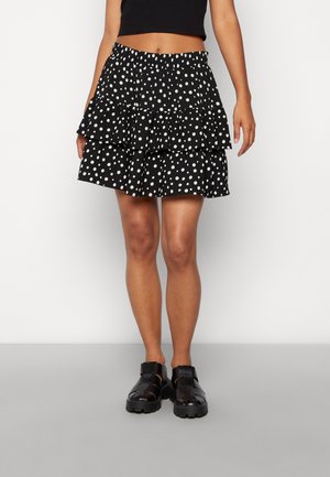 Kvinde iført et sort lagdelt skørt med hvide prikker, sammen med en sort crop top og sorte chunky lukkede sandaler.
